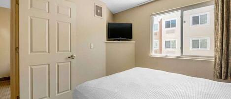 Una habitación de hotel con una cama, un televisor sobre un mueble, una ventana con cortinas y una puerta.