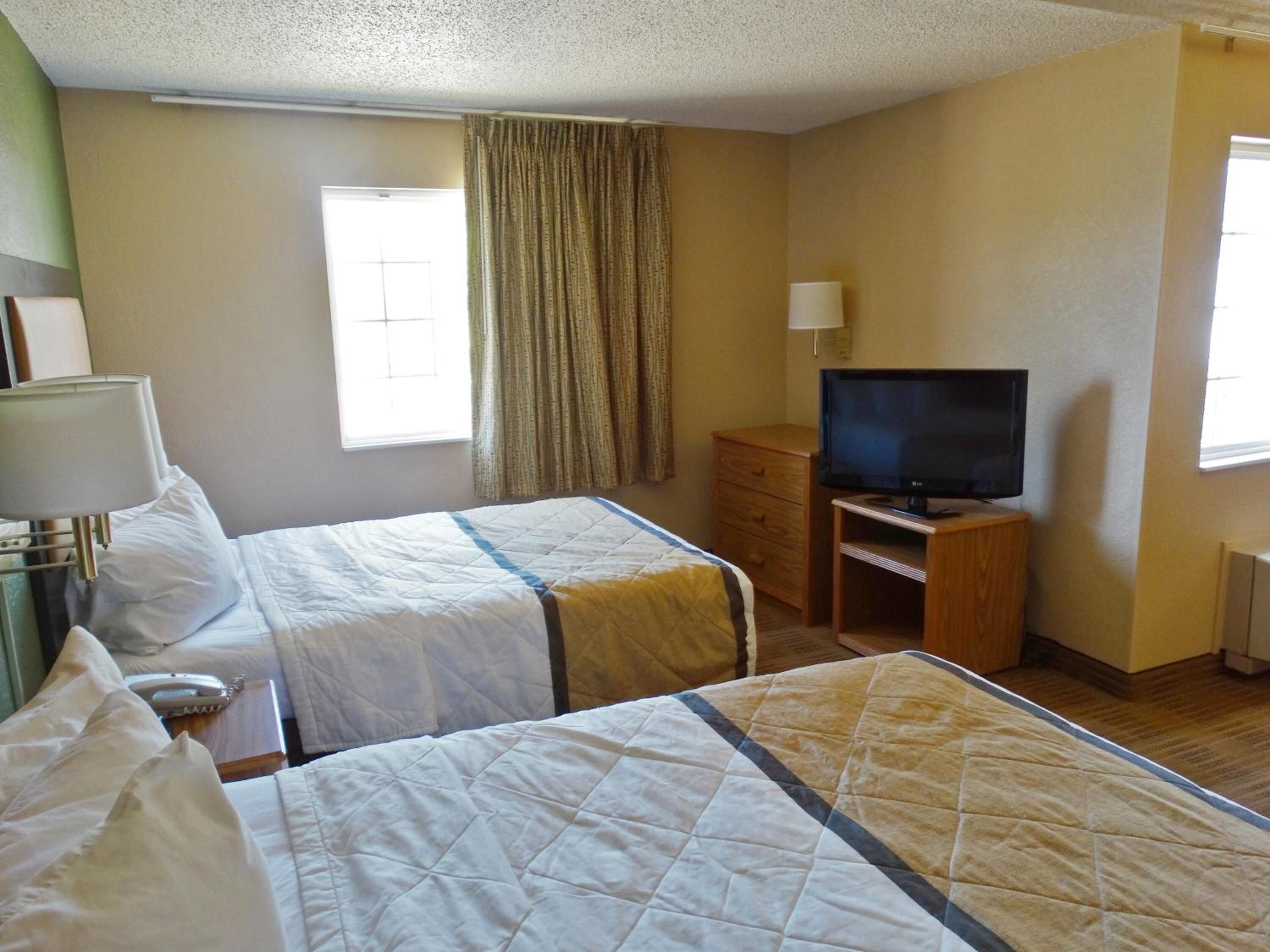 A hotel room with two beds, a TV, a desk, and a window with curtains.