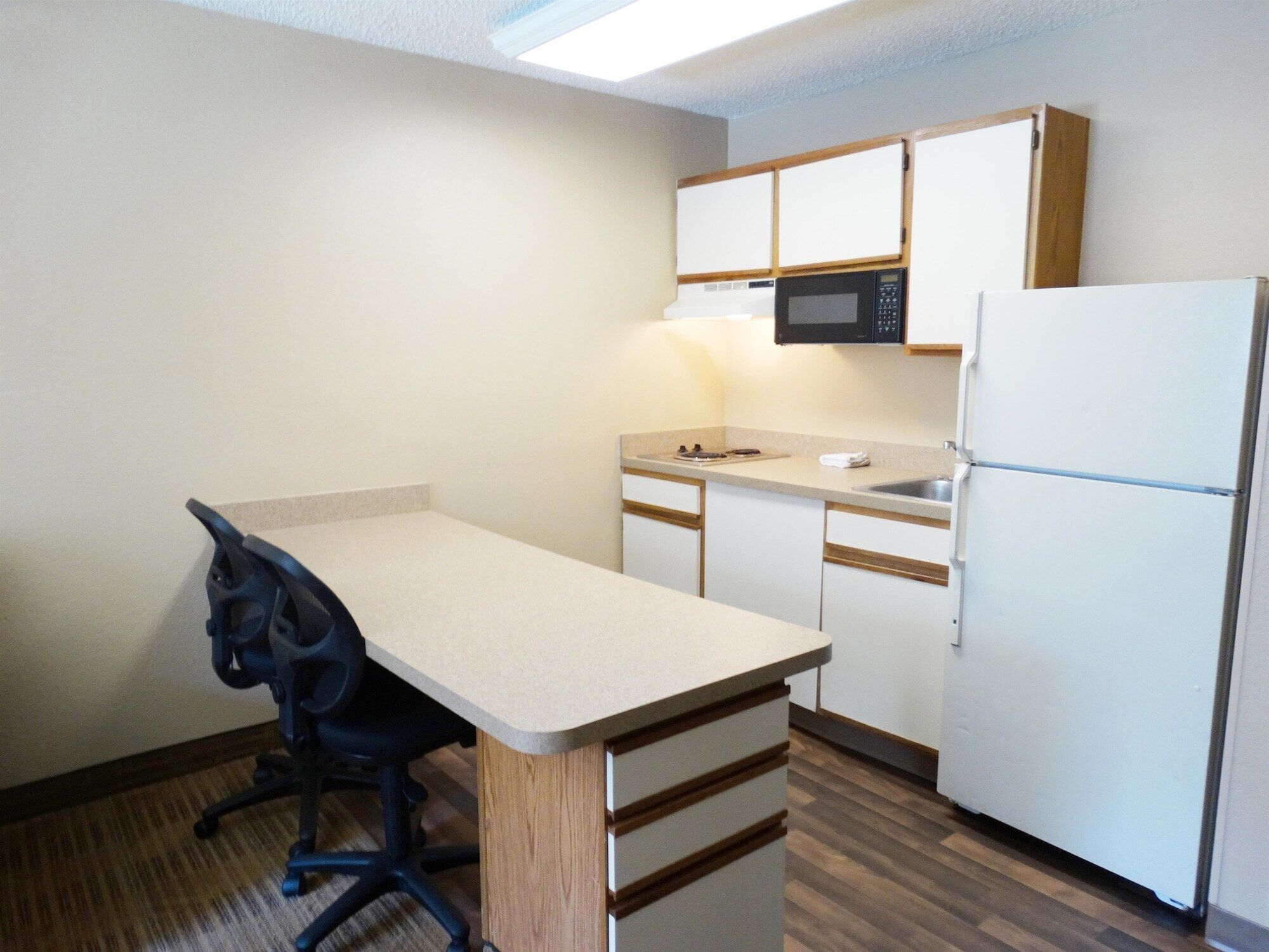 A compact kitchen with a single countertop, a microwave, a refrigerator, and a chair.