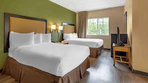 A hotel room with two beds, a TV on a stand, and a window with a view of trees.