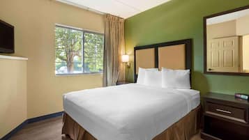 Una habitación de hotel con una cama grande, una mesita de noche, una lámpara, una ventana con cortinas y un televisor en la pared.