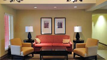 A lobby with a red sofa, two armchairs, a coffee table, and two lamps. There are framed pictures on the wall.