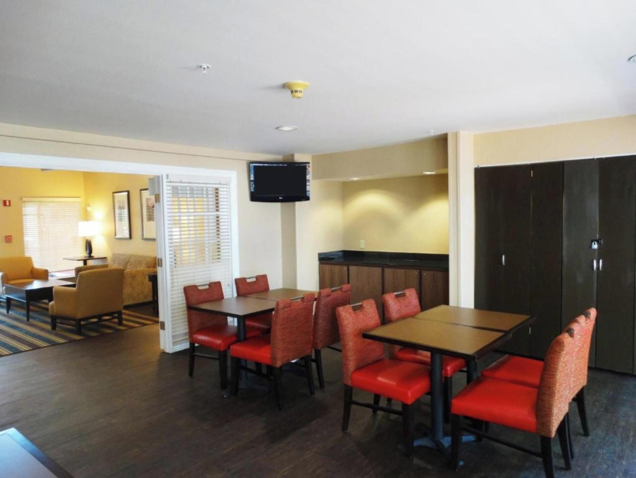 A hotel room with a dining area, a TV mounted on the wall, and a kitchenette.