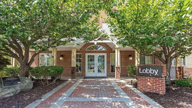 A brick building entrance with a sign reading 'Lobby,' surrounded by trees and a paved walkway.