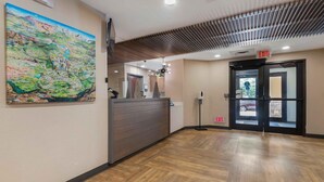 A hotel reception area with a wooden floor, a large painting on the wall, and a double door with an exit sign. - Extended Stay America Suites Charlotte Pineville Park Rd (Pineville)