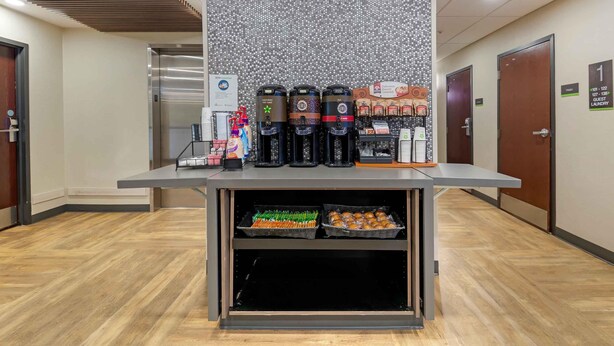 Zona de recepción de hotel con estación de café, lavandería para huéspedes y una pared con diseño moteado.