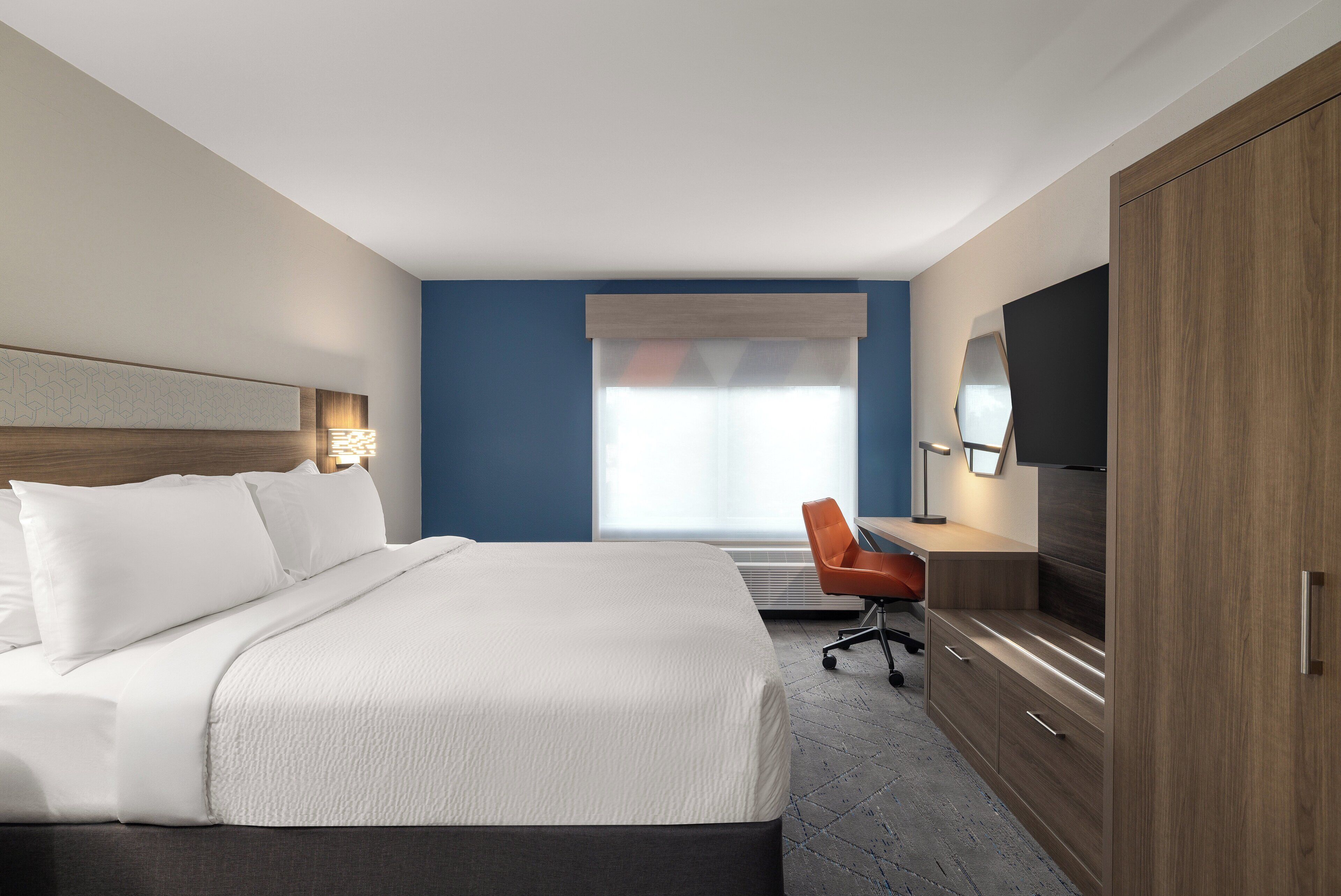A hotel room with a large bed, a desk, a chair, and a TV.