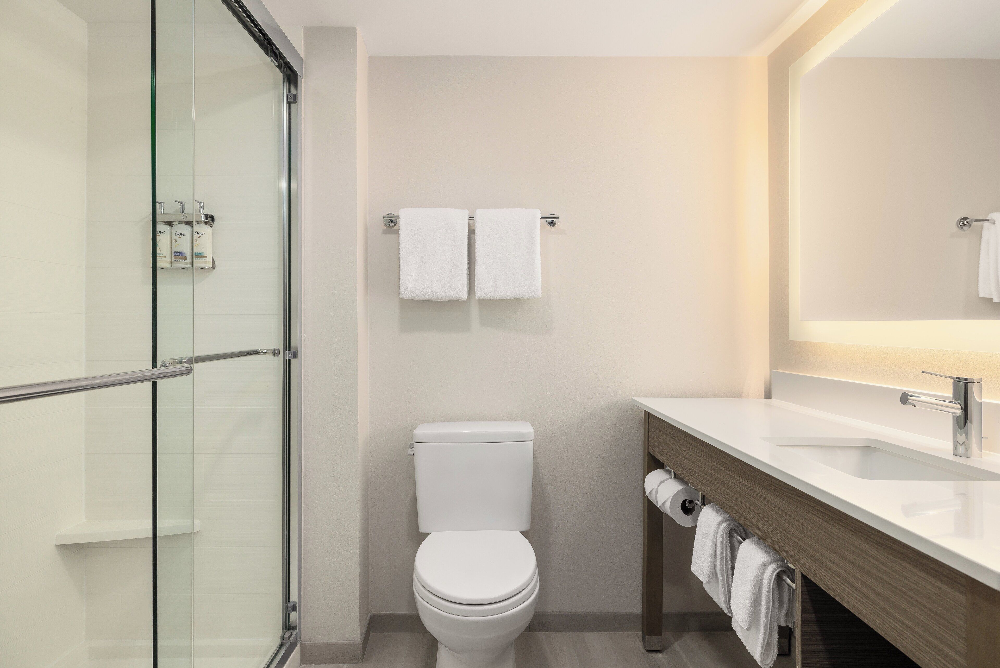 Un baño moderno con cabina de ducha de vidrio, inodoro blanco y tocador de madera con espejo.