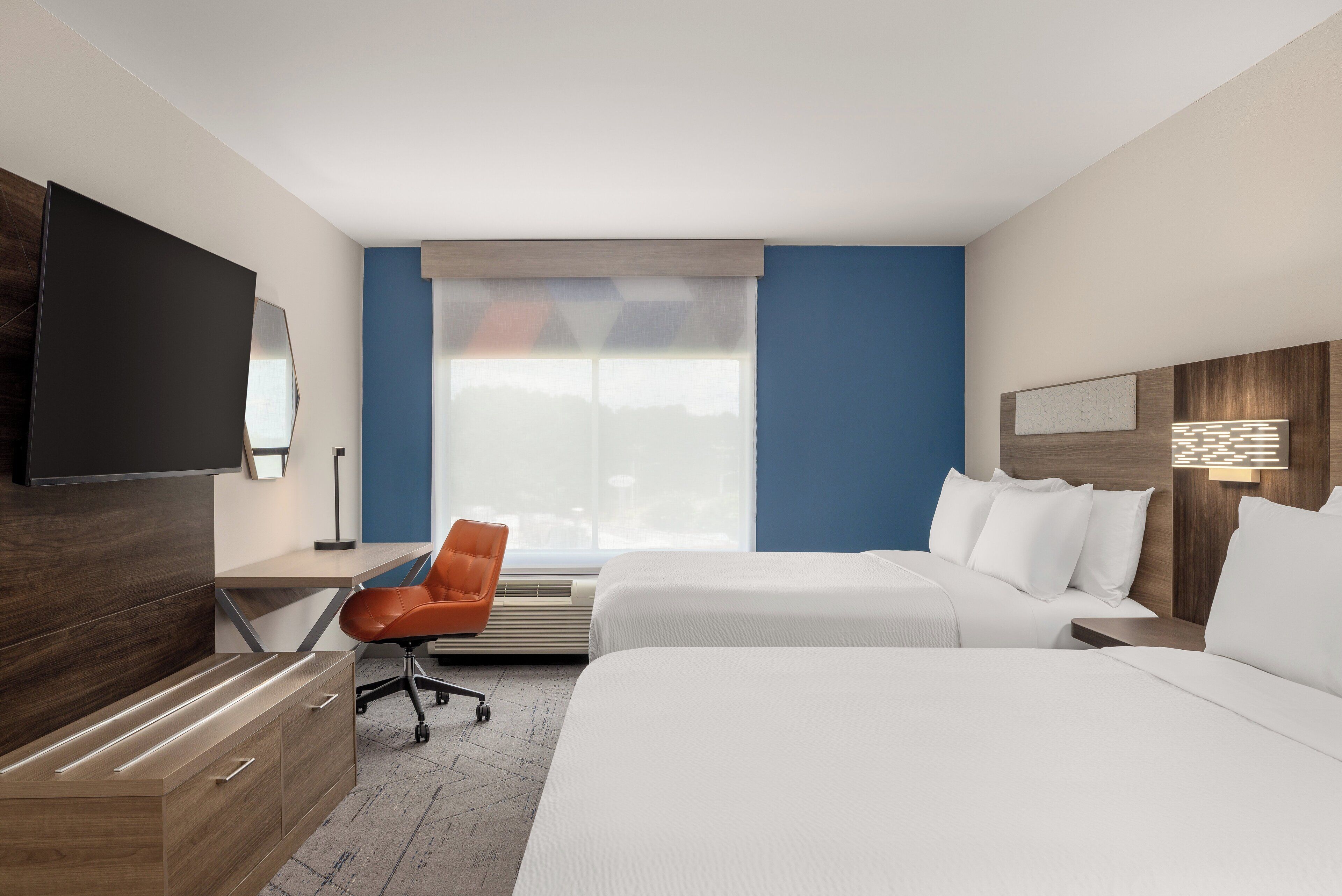 A hotel room with two beds, a desk, a chair, a TV, and a large window.