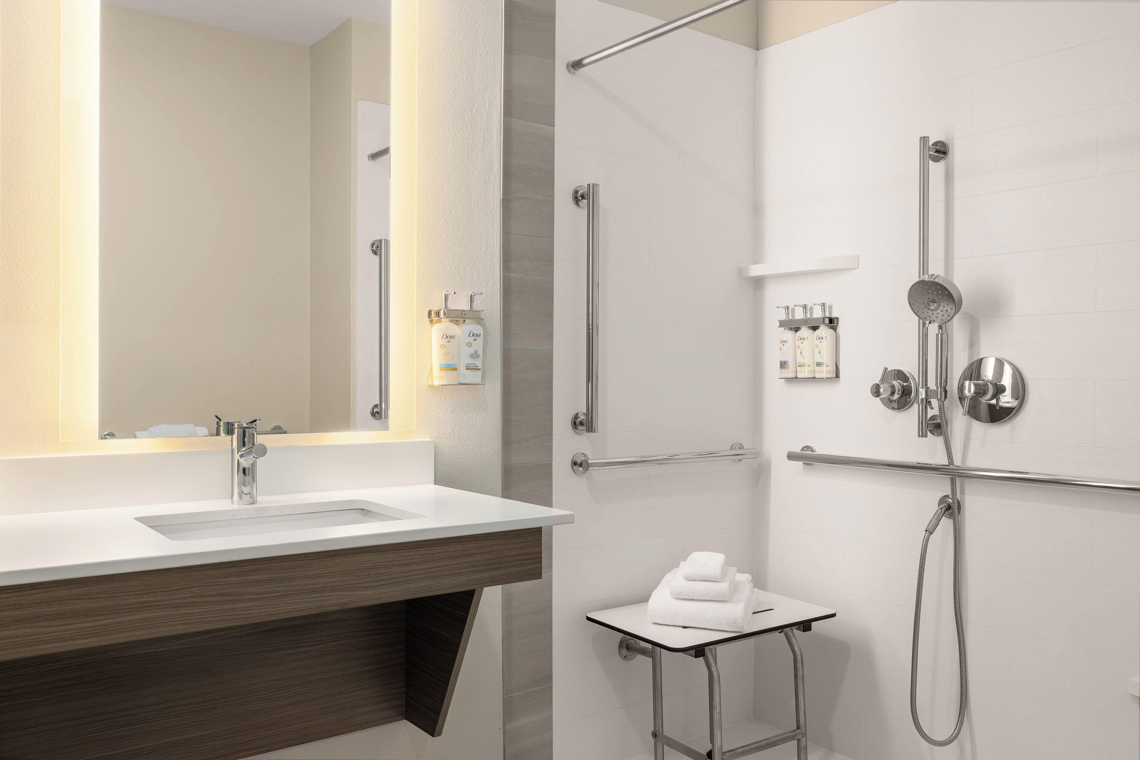 Un baño moderno con lavamanos, espejo, ducha y tendedero para toallas.