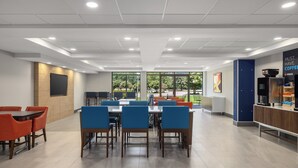 A modern dining area with tables and chairs, a coffee station, and large windows offering a view of greenery. - Holiday Inn Express Fayetteville – Fort Bragg by IHG (Fayetteville)