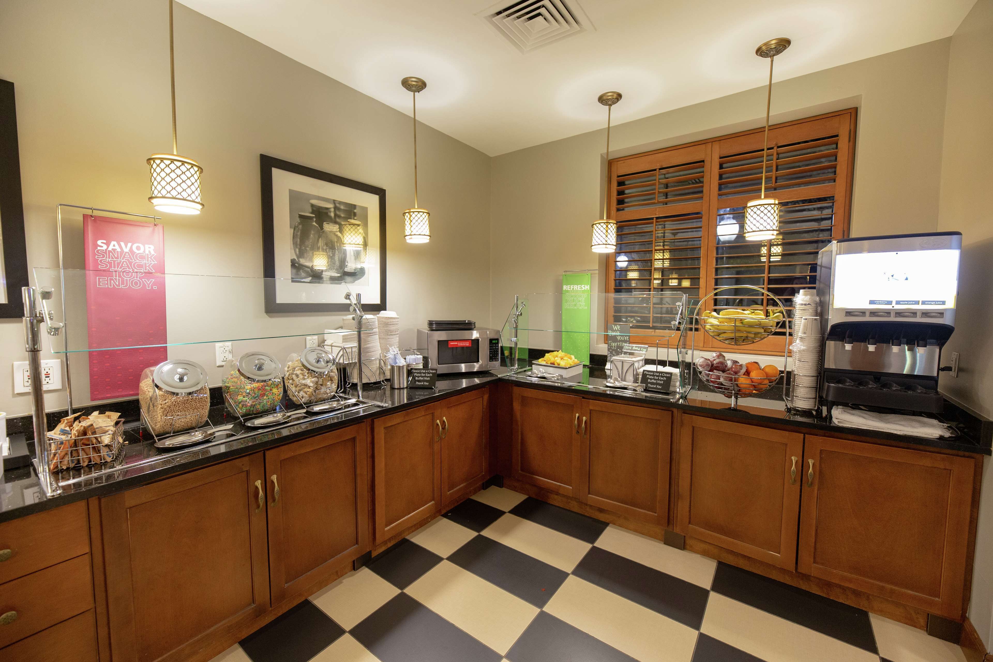 A hotel kitchen with a checkered floor, wooden cabinets, a microwave, and various food items on the counter.
