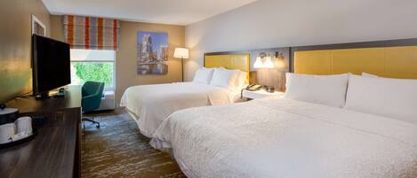 A hotel room with two beds, a desk with a television, and a window with blinds.