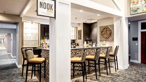 A bar area with a sign reading "The Nook Bar," featuring a counter with bottles and a menu, surrounded by four bar stools with cushioned seats. - Hampton Inn & Suites Raleigh Cary Lenovo Center (Raleigh)