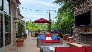 An outdoor patio with wicker furniture, a red umbrella, and string lights. - Hampton Inn & Suites Raleigh Cary Lenovo Center (Raleigh)