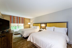 A hotel room with two beds, a TV, a desk, and a window with blinds.
