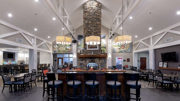 A spacious bar area with a stone fireplace, multiple seating arrangements, and a television. - Hampton Inn & Suites Raleigh Cary Lenovo Center (Raleigh)