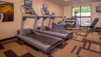 A gym with treadmills, a bench, and dumbbells.