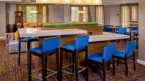 Un hall de hotel con una zona de bar central, diversas disposiciones de asientos y una alfombra estampada.