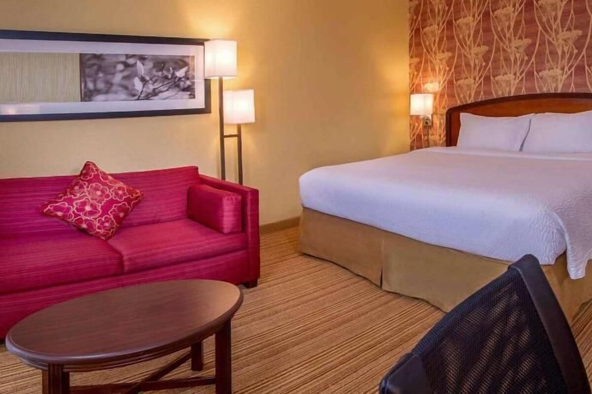 Ein Hotelzimmer mit einem Bett, einer roten Couch, einem kleinen Tisch und einem Sessel.