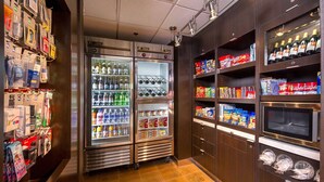 Zona de venta con dispensadores de bebidas frías, estantes con aperitivos y un microondas.