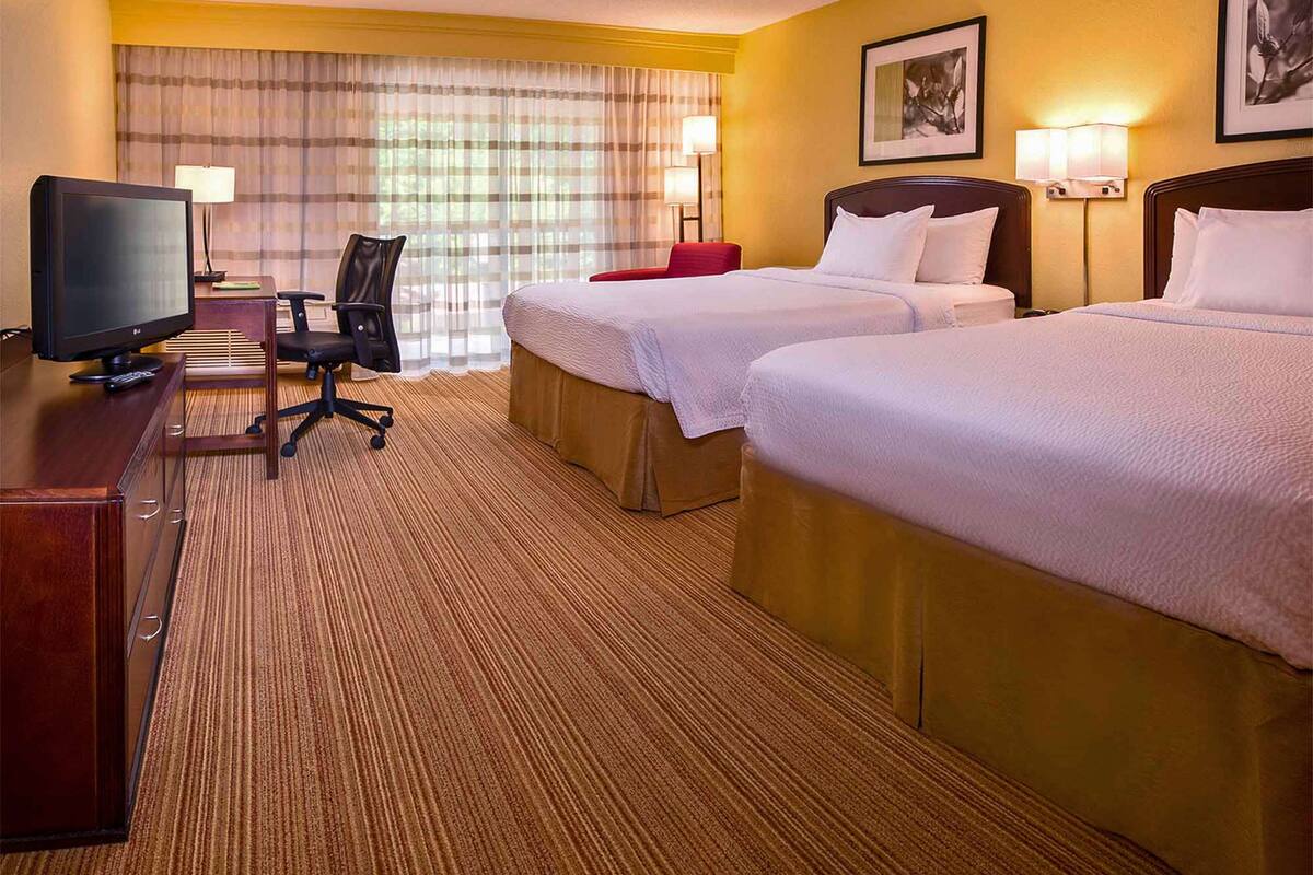 A hotel room with two beds, a desk with a TV, a chair, and a lamp.