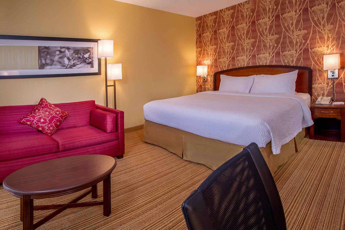A hotel room with a bed, a red sofa, a small table, and two bedside lamps.