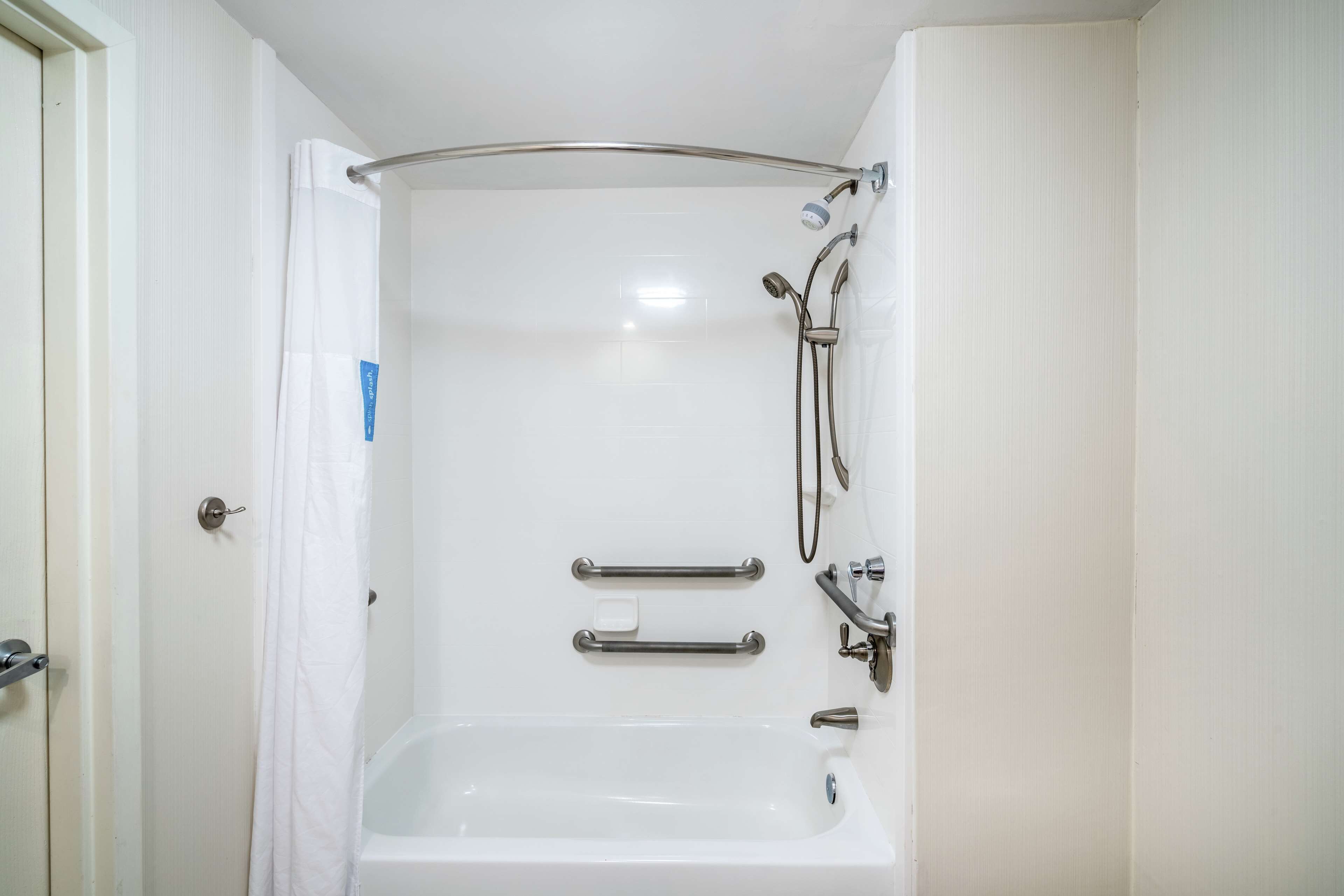 A bathroom with a bathtub, shower, and grab bars.