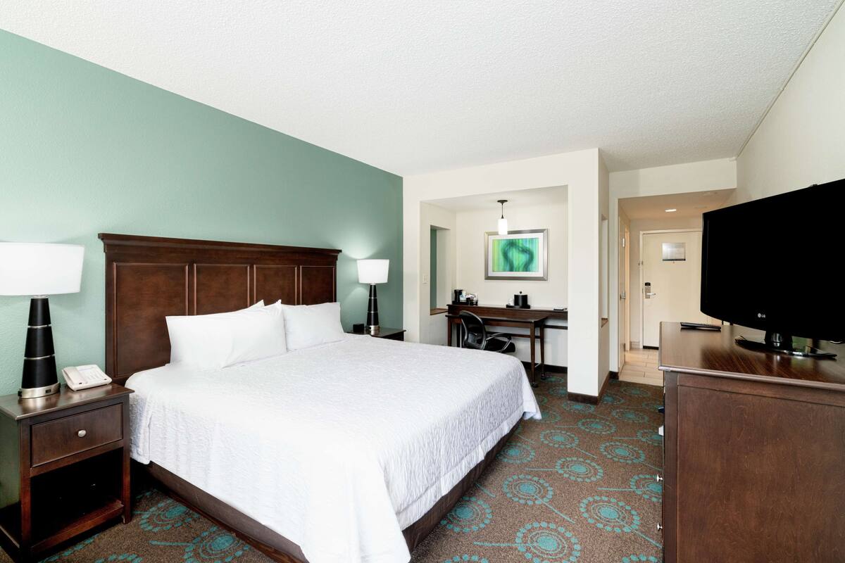 A hotel room with a large bed, a desk, a television, and a desk lamp.