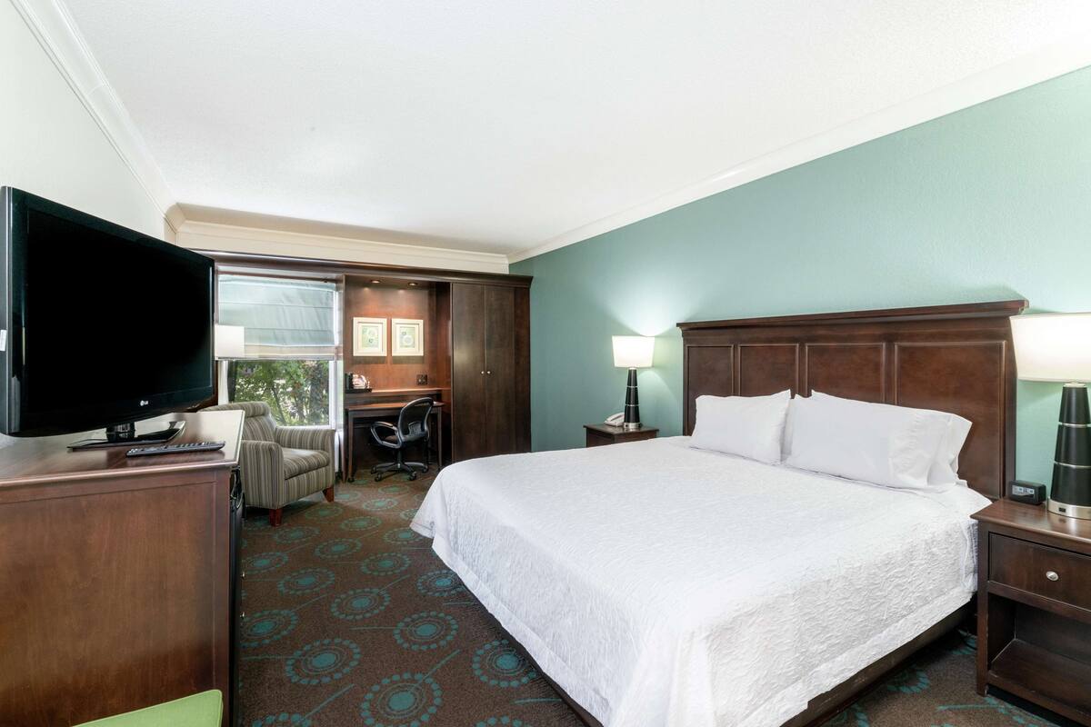 A hotel room with a large bed, a desk with a chair, a television, and a window.