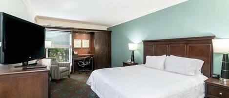 A hotel room with a large bed, a desk with a chair, a television, and a window.