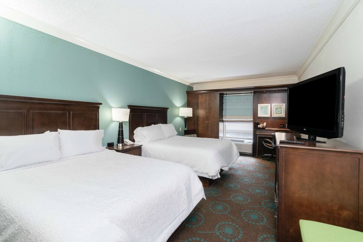 A hotel room with two beds, a desk, a television, and a bathroom visible through an open door.