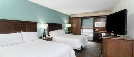 A hotel room with two beds, a desk, a television, and a bathroom visible through an open door.