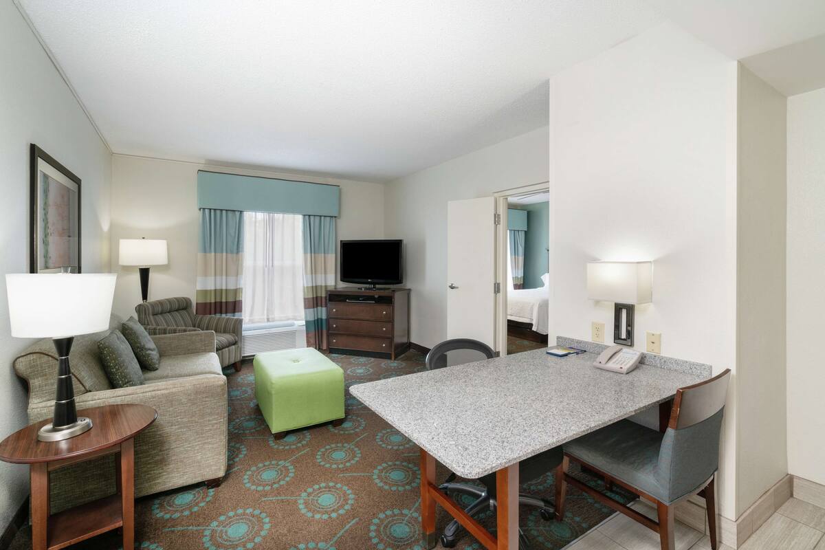 A hotel room with a bed, a desk, a chair, a television, and a sofa.