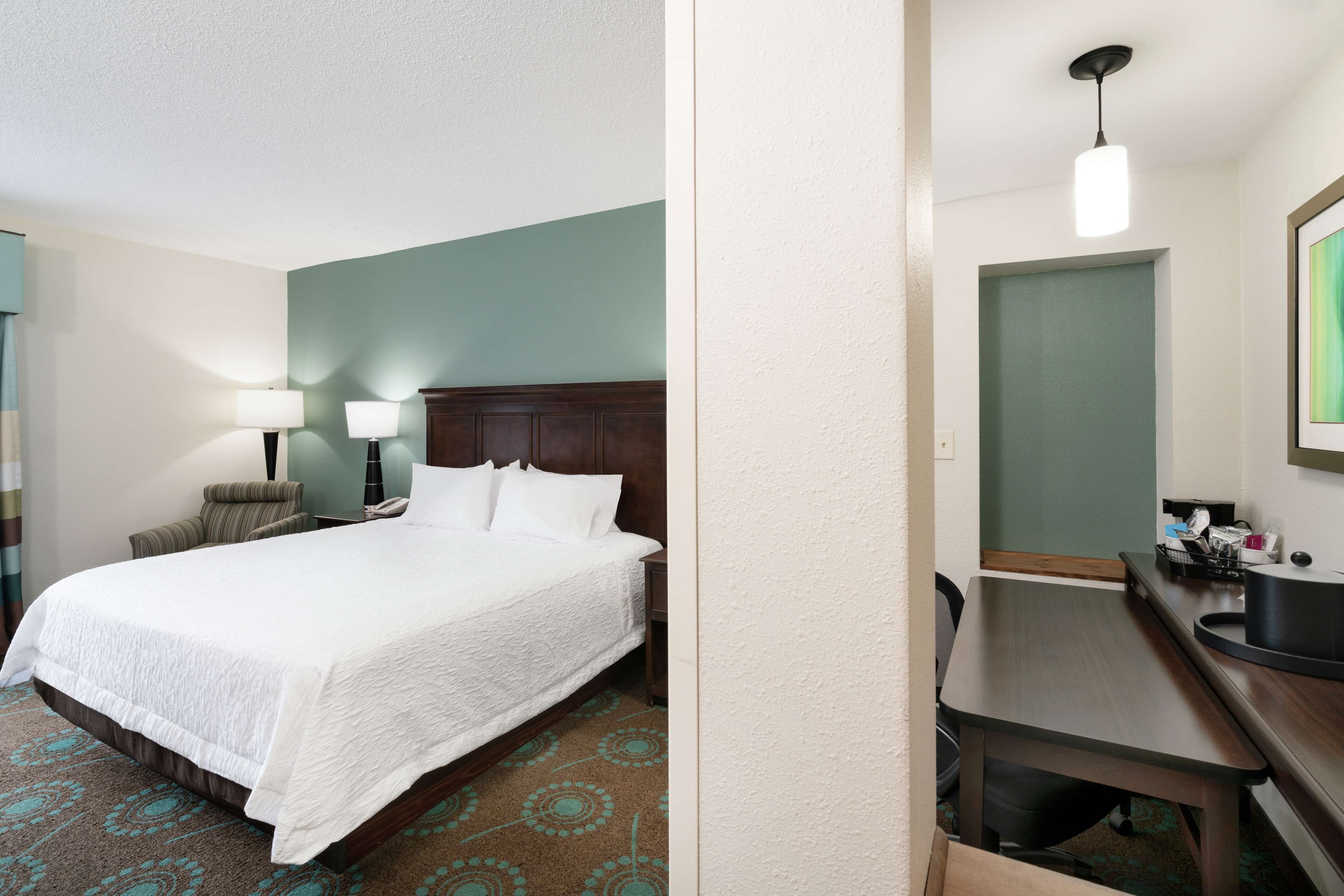 Une chambre d’hôtel avec un grand lit, un bureau, une chaise, une lampe et un miroir.