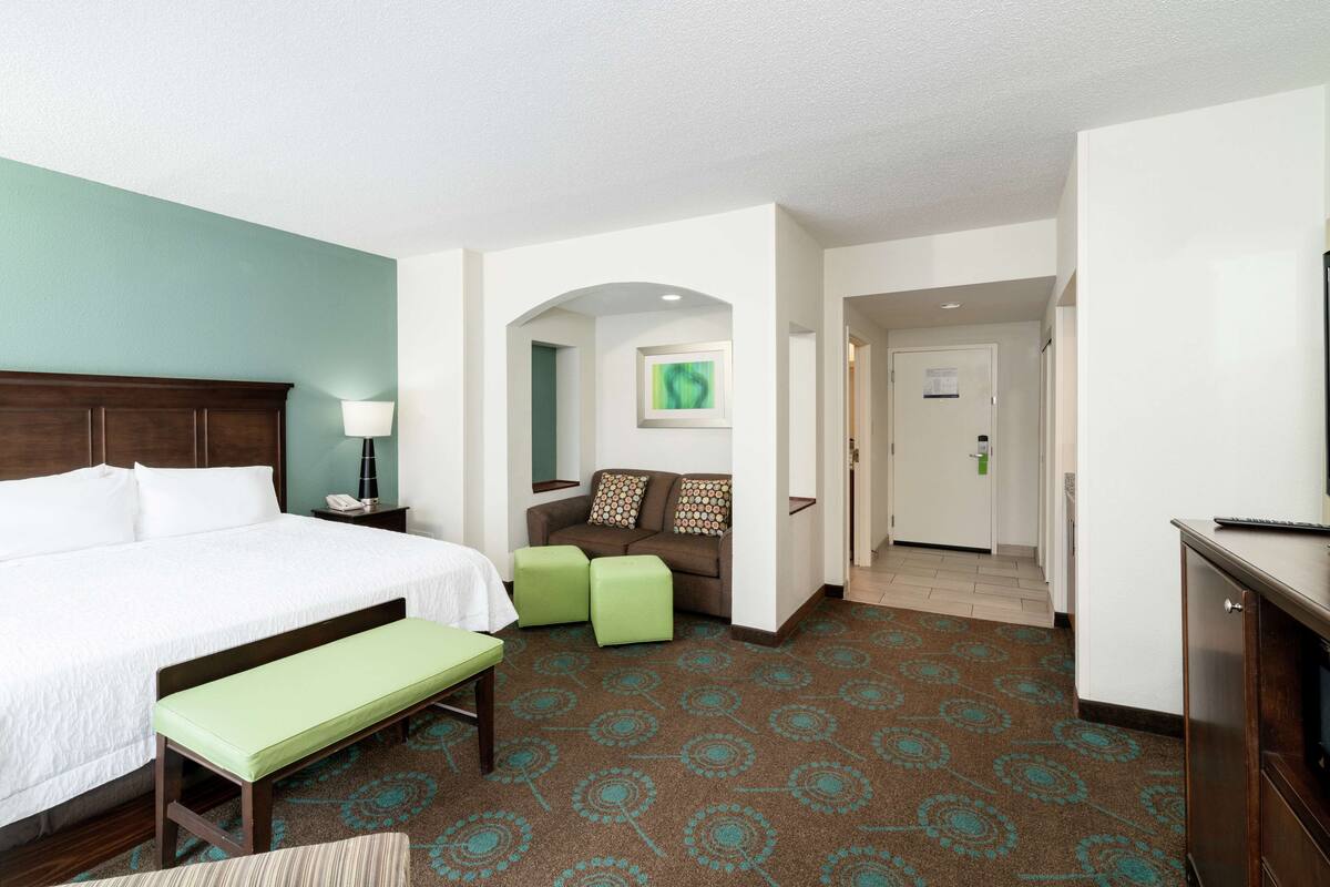 A hotel room with a large bed, a bench, a sofa, and a desk.