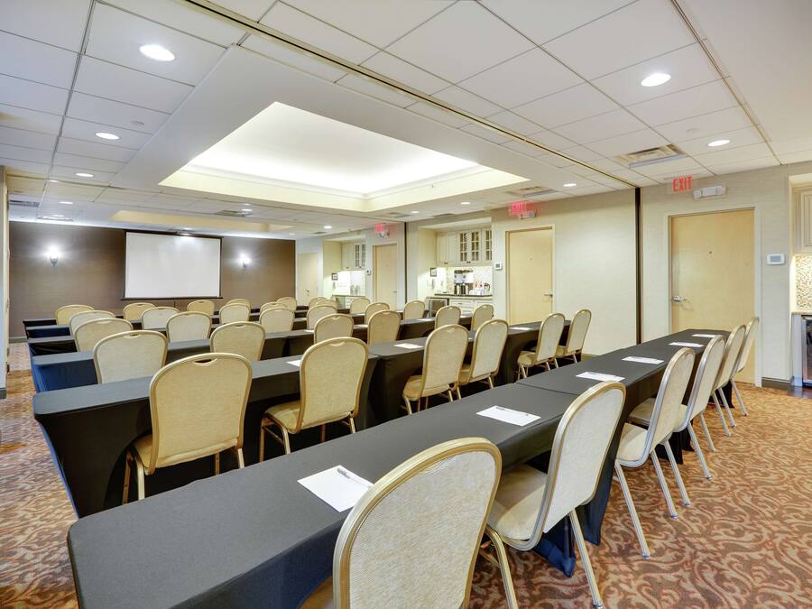A conference room with multiple tables and chairs, a projector screen, and an exit sign.