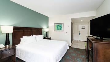 A hotel room with a large bed, a TV, a desk with a lamp, and a painting on the wall.