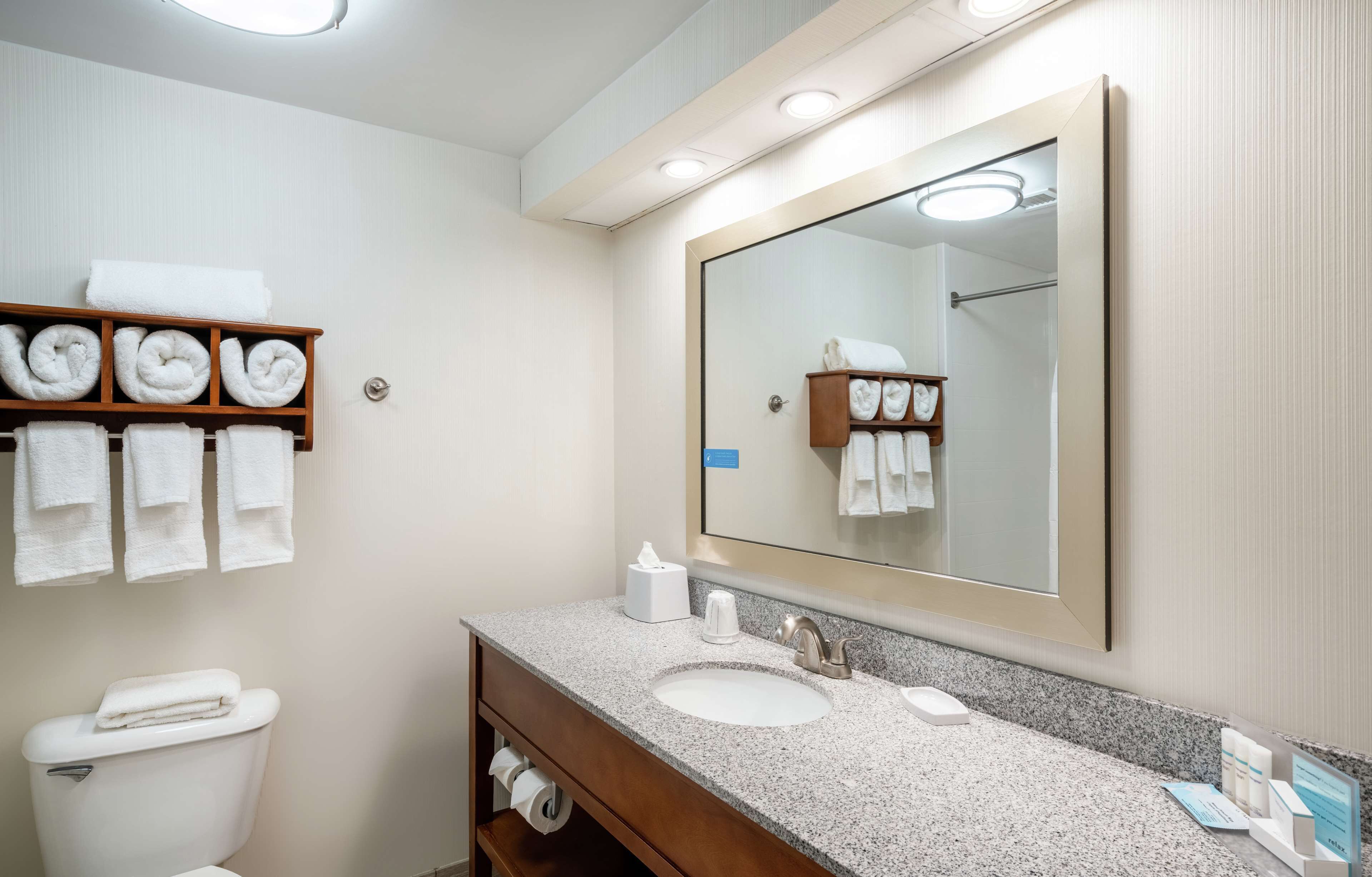 A hotel bathroom with a large mirror, two sinks, a towel rack, and a toilet.