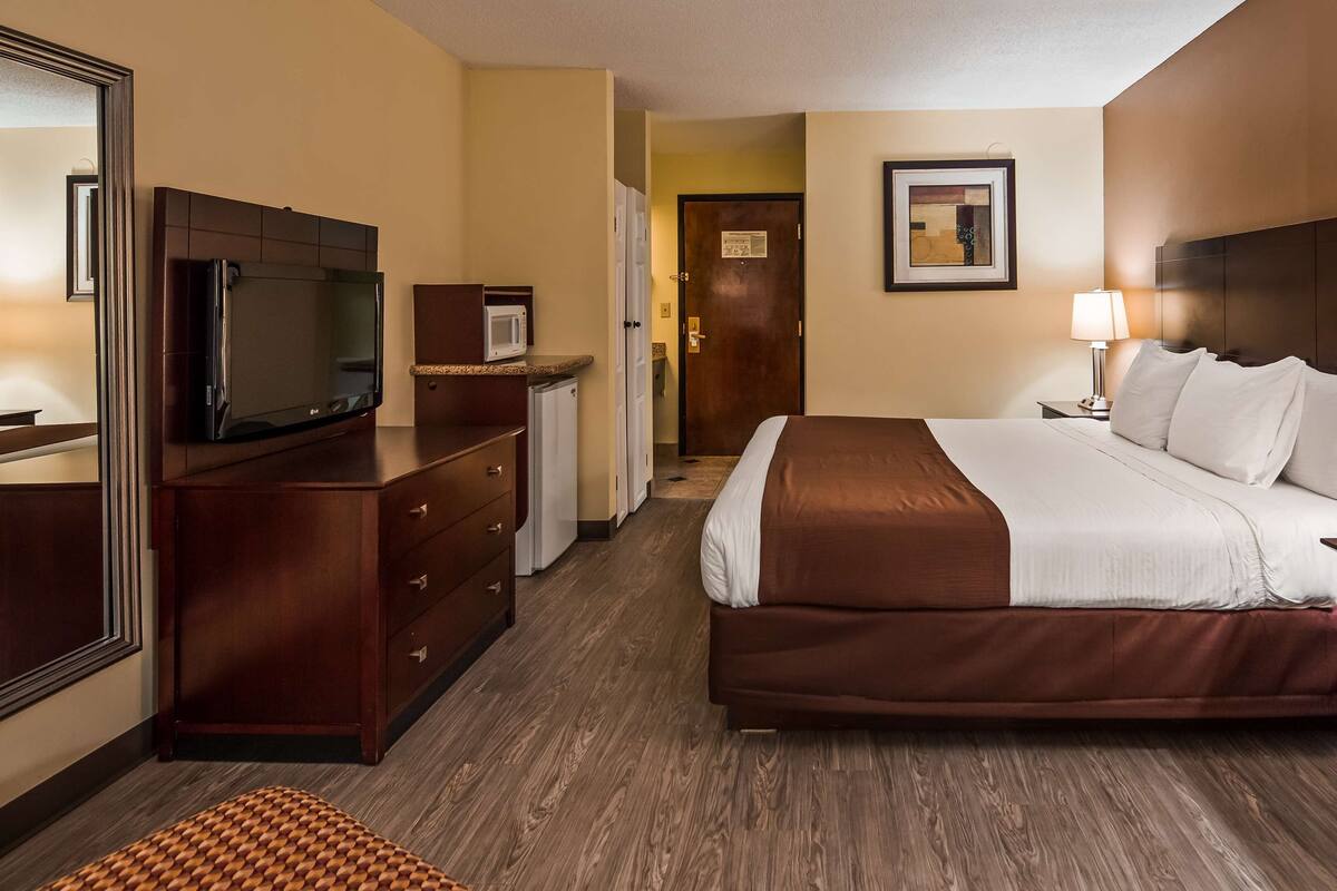 Ein Hotelzimmer mit einem großen Bett, einem Fernseher, einer Mikrowelle, einem Schminktisch und einer Tür zu einem Flur.