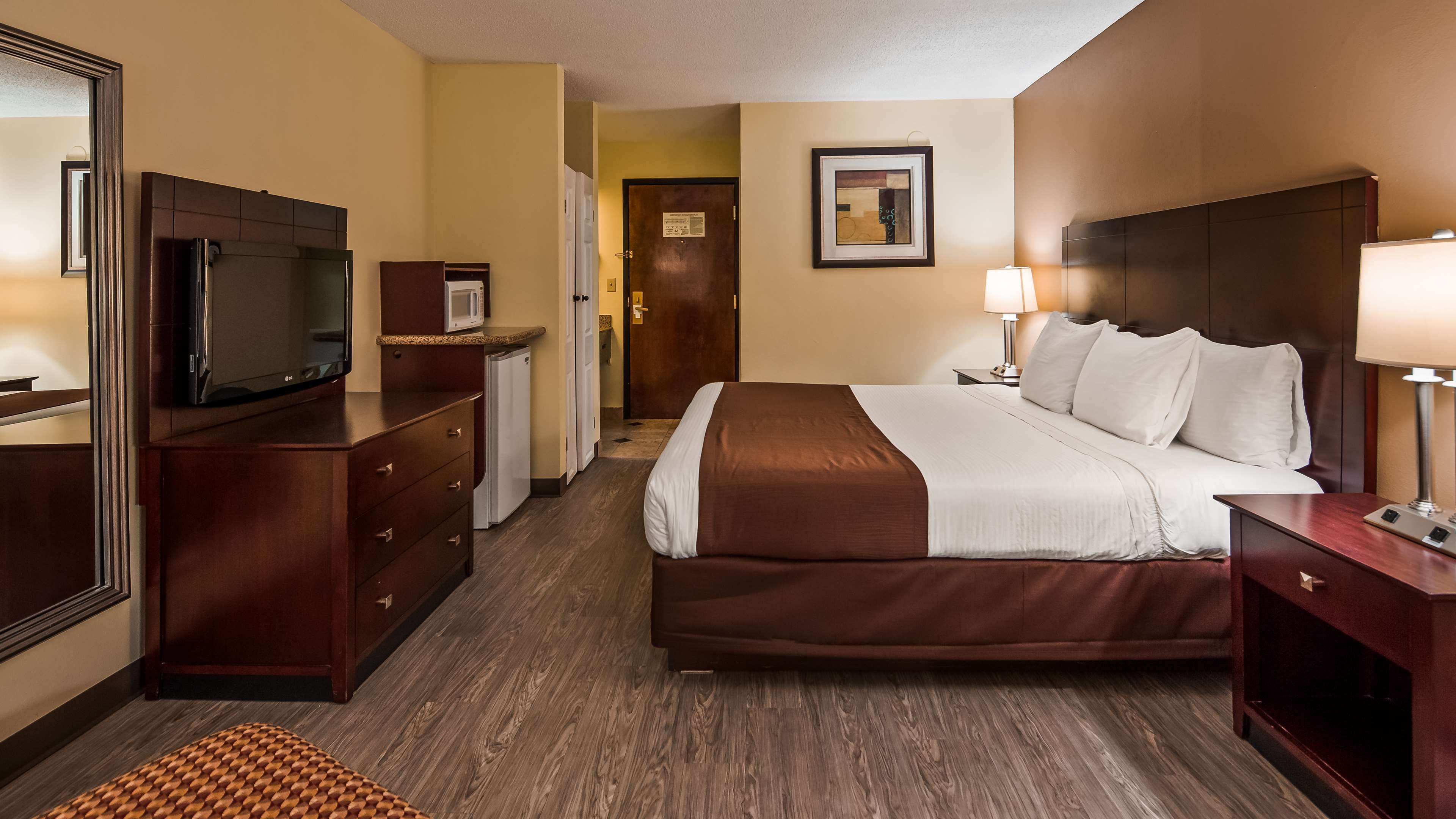 Habitación de hotel con una cama grande, televisión, microondas, cómoda y puerta que da a un pasillo.