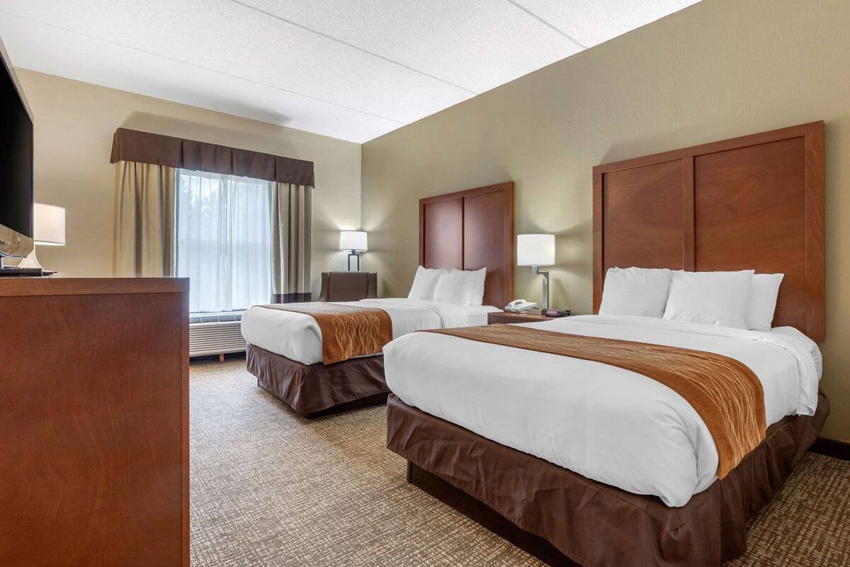 A hotel room with two beds, a desk, a lamp, and a window with curtains.