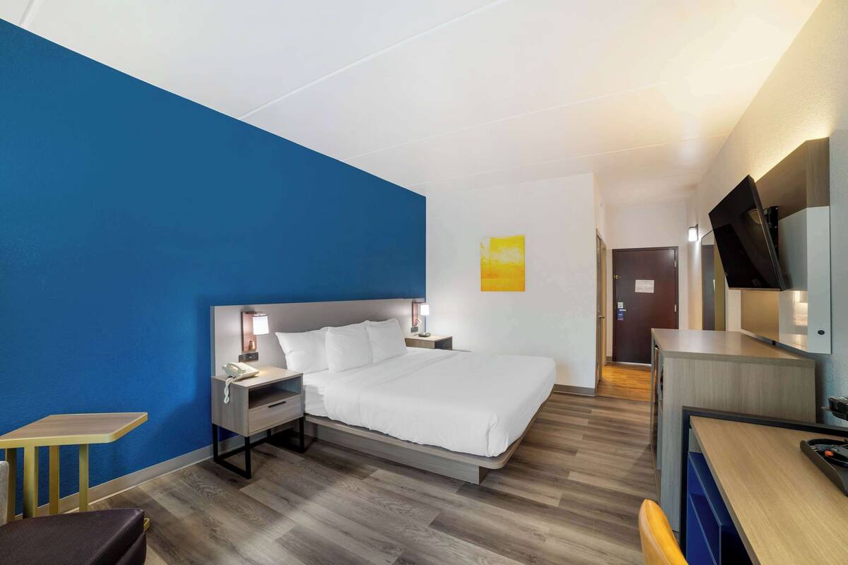 A modern hotel room with a large bed, bedside tables, a desk, and a television.