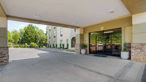 Entrada de hotel con un vestíbulo techado, estacionamiento y un edificio con toldo verde.