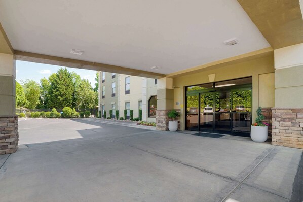 A hotel entrance with a covered walkway, a parking lot, and a building with a green awning. - Comfort Inn Asheville Airport (Fletcher)