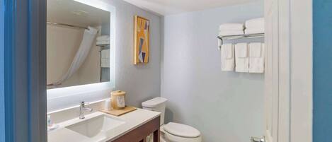 Baño con lavamanos, espejo, inodoro y toallero.