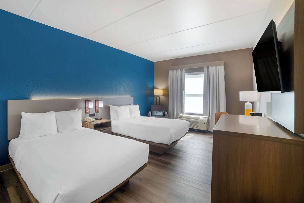 A hotel room with two beds, a desk, a TV, and a window with curtains.