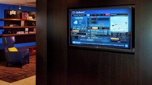A GoBoard® display in a hotel lobby with a dark wood panel, a blue chair, and a bookshelf. - Courtyard by Marriott Cleveland Westlake (Westlake)