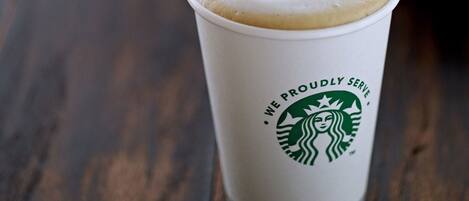 A Starbucks cup with a frothy top on a wooden table.