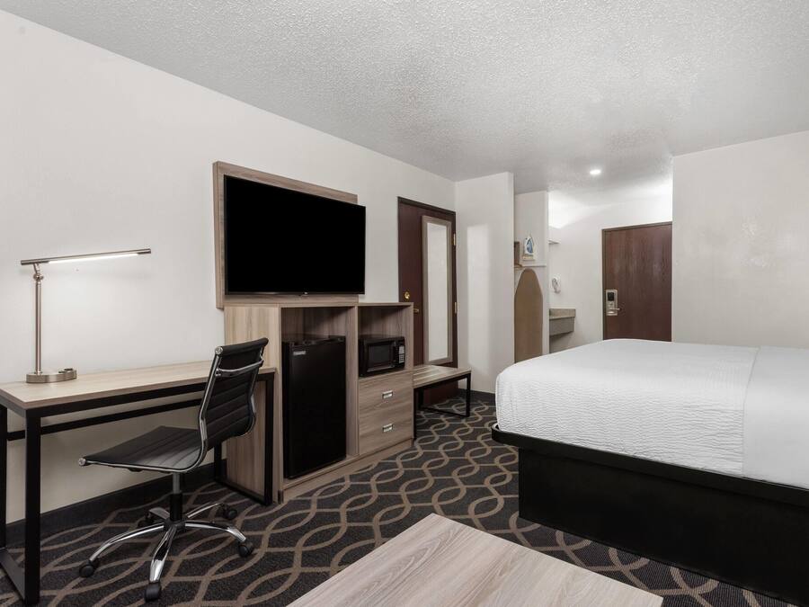 Habitación de hotel con cama, escritorio, silla, televisión y armario.